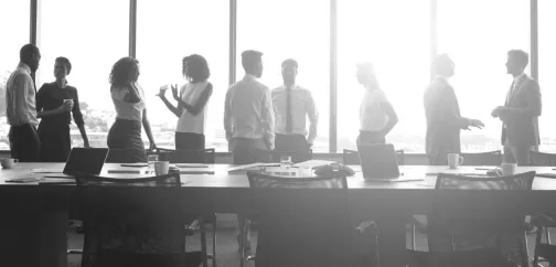 A board meeting with lots of people stood around a table